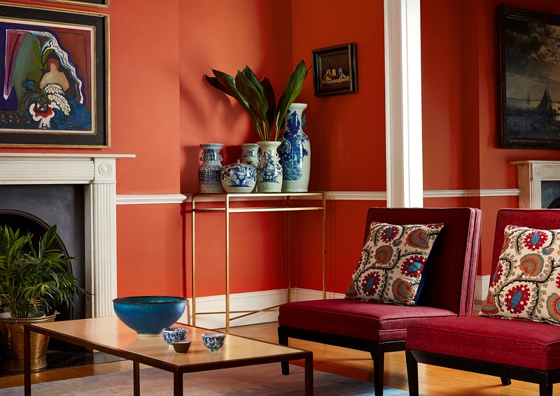 Deep orange walls with red chairs and patterned cushion in lounge